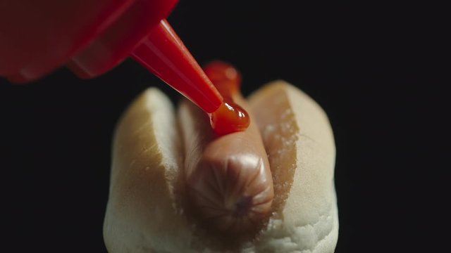 Ketchup bottle pouring tomato sause on a hot dog with sausage. Close up