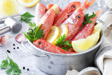 Fresh striped red mullet in a tin basket with slices of lemon and parsley leaves