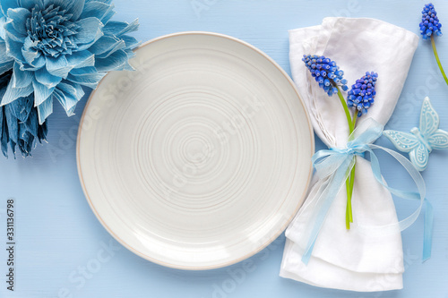 Table place setting with an empty plate and a folded napkin decorated with blue spring flowers and ribbon. Mother's Day or Wedding dinner concept