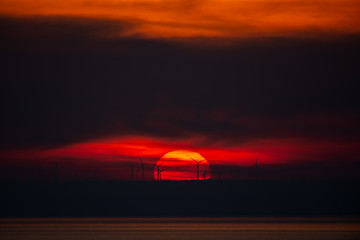 Sun setting behind wind turbines with clouds around