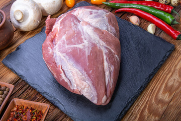 a piece of fresh pork meat with spices, vegetables, on a rustic wooden table