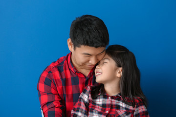 Happy Asian man and his little daughter on color background