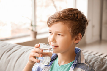 Cute little boy drinking water at home