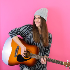 Young smiling woman playing music on acoustic guitar, over vivid pink background. Girl guitar player