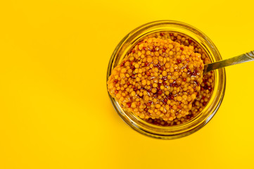 French mustard in a glass jar, shot on a yellow background. Background for seasoning and nutrition.