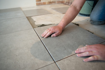 Tiler laying the ceramic tile on the floor. Professional worker makes renovation. Construction. Hands of the tiler. Home renovation and building new house