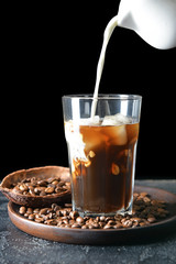 Pouring of milk into cold coffee in glass on table