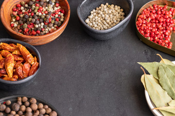 Different  spices , pepper type, black ,white, pink ,green, cayenne, allspice peppercorns and bay leaf in bowls on dark background.Copy space