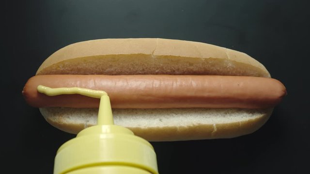 TOP VIEW: Yellow mustard sause poring on a hot dog with sausage from a bottle.