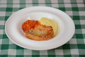Fried fish filet with mashed potatoes and tomato sauce served on white plate on wooden table.
