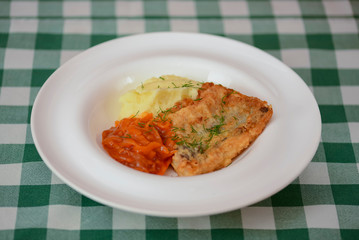 Fried fish filet with mashed potatoes and tomato sauce served on white plate on wooden table.