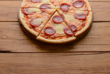 Flat lay pepperoni pizza isolated on rustic wooden background. Pizza salami cut in slices. Fast food, junk food concept.