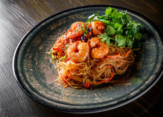 Stir fry noodles with vegetables and shrimps in plate on wooden table background