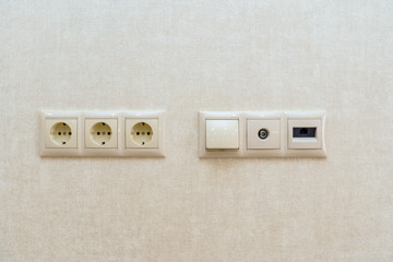 three electrical outlets on the wall against a background of sand colored Wallpaper with a pattern of oval lines