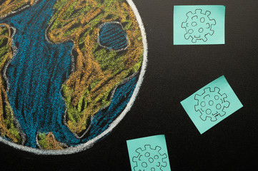Planet earth is drawn by children on a blackboard with chalk, around a virus, a threat to the planet, a pandemic and an epidemic. Coronavirus