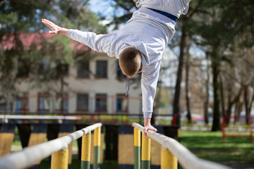 A man does exercises on uneven bars on the street. A man goes in for sports.