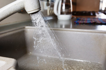 Water is pouring from a faucet. Water tap on the background of the kitchen. Water saving.