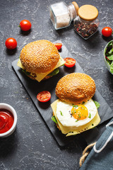 Breakfast two burgers with chicken, fried egg and cheese on a dark stone background