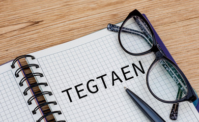 the word TEGTAEN is written in a notebook with glasses