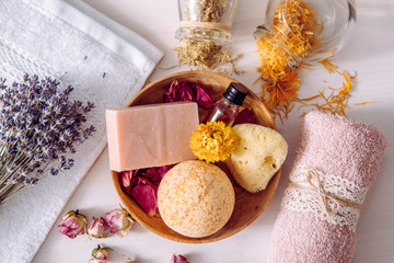 Various organic dried herbs flower petals used in beauty bath products concept. Top view of bath bomb, natural sea sponge, bar of soap, aroma oil bottle and jars with scattered dry herbs around.