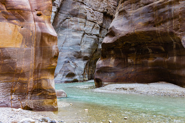 Wadi Mujib Nature Reserve in Jordan. Mujib Canyon near Dead Sea coastline. River flows between sheer cliffs of canyon. Colorful rocks go vertically up.