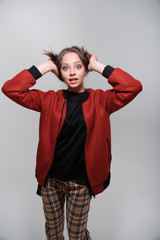 Portrait of a young funny girl in a black T-shirt and a red bomber jacket.The girl holds on to her hair and fools around, grimaces