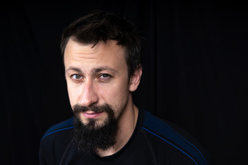 a close up portrait of a young man with beard in dark clothes on a dark background