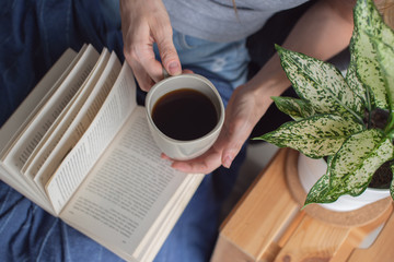 Woman holding a cup and reading a book.