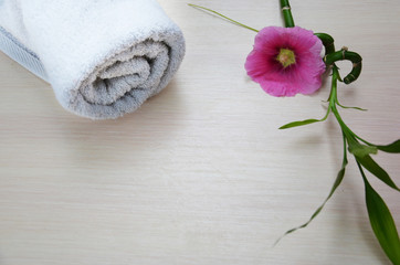 background of a spa with pink flower, white towel rolled up and a sprig of green bamboo
