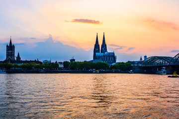 Fototapeta premium Sunset silhouette skyline landscape of the gothic Cologne Cathedra, Hohenzollern railway and pedestrian bridge, the old town and Great St Martin church on the banks of river Rhine in Cologne, Germany