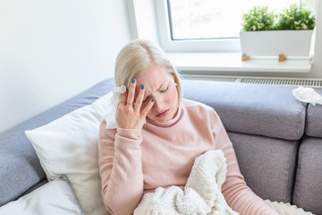 Sick woman with headache sitting under the blanket. Sick woman with seasonal infections, flu, allergy lying in bed. Sick woman covered with a blanket lying in bed with high fever and a flu, resting.