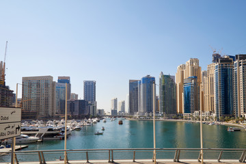 Dubai Marina skyscrapers and boats in harbor in a sunny day, clear blue sky in Dubai, United Arab Emirates