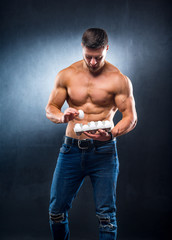 Handsome young sportsman is holding a packaging with eggs, healthy food protein, gray background. Naked torso, healthy life concept.