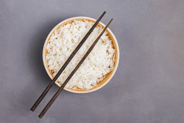 Bowl of cooked jasmine rice and chopsticks on gray table
