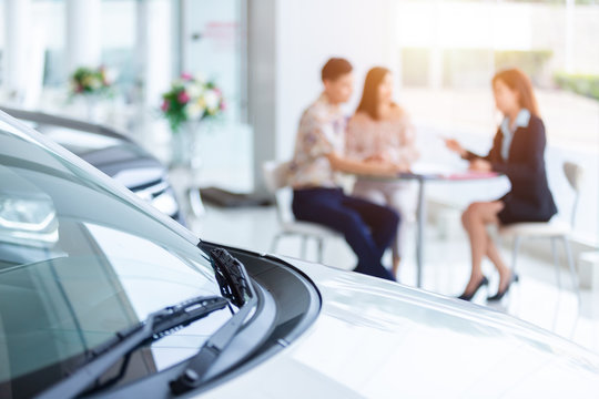 Selective focus on a new car and blur the dealership professional salesman and couple purchasing brand new car. concept professionalism agreement contract leasing renting retail car sales.