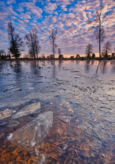 A cold sunset in winter on a frozen lake with a beautiful sky and sunbeams in the background Friesland, The Netherlands