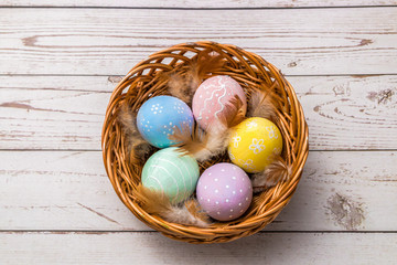 top view of easter eggs hand painted in pastel colors and tender feathers in a wicker basket on wooden table