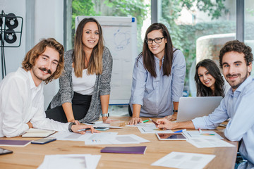 Teamwork - Portrait of a group of colleagues in a meeting in an office room at a wooden table - Millennials of a young start-up - Concept of hard work
