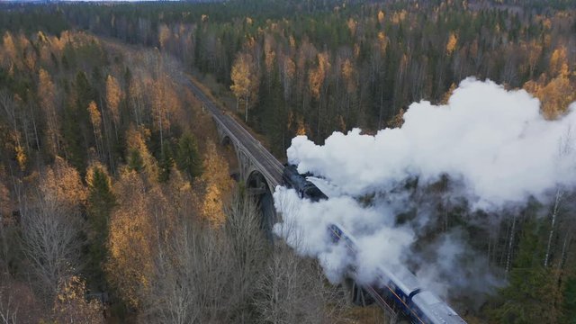 Aerial view steam train pass over the bridge in forest. Retro locomotive with blue car running on railroad