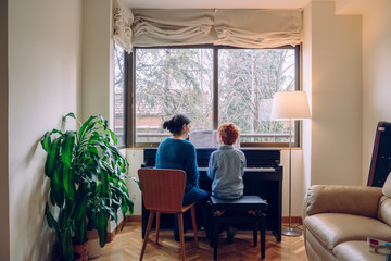 Mom teaching her son at home piano lessons. Family lifestyle spending time together indoors. Children with musical virtue and artistic curiosity. Educational musical activities for little kid.