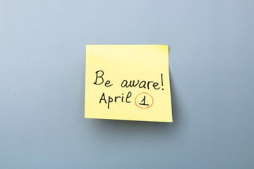 be aware on yellow sticky note over a grey background. april fools day