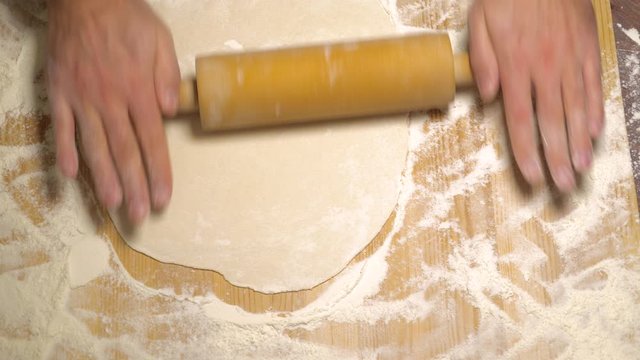 Man rolls out the dough on the kitchen table. Male hands rolling dough with a rolling pin, close up. Man cooking food at home. Men hands roll a dough rolling pin. Service to woman. Real time 4k