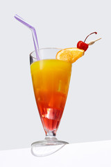 Sex on the Beach cocktail with ice cubes is contained in a milkshake glass with a straw, an orange slice and a cherry on the stick. The showy illustrative picture is made on the gray backdrop.