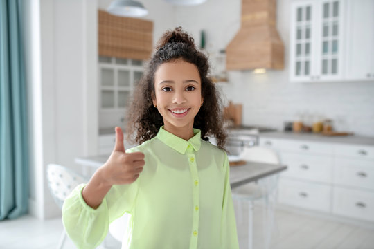 Dark-haired girl with curly hair smiling showing thumb up