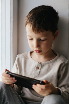 Toddler boy using tablet or smartphone. Cute five years old boy sitting at home using digital device.