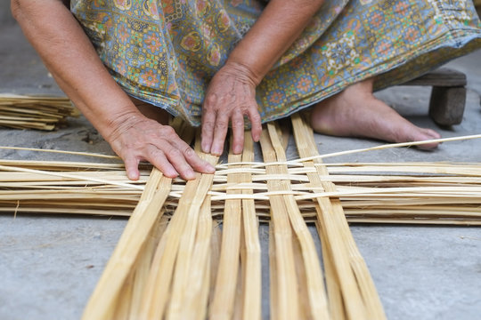Hand elderly woman are weave bamboo strips of bottom of basket.