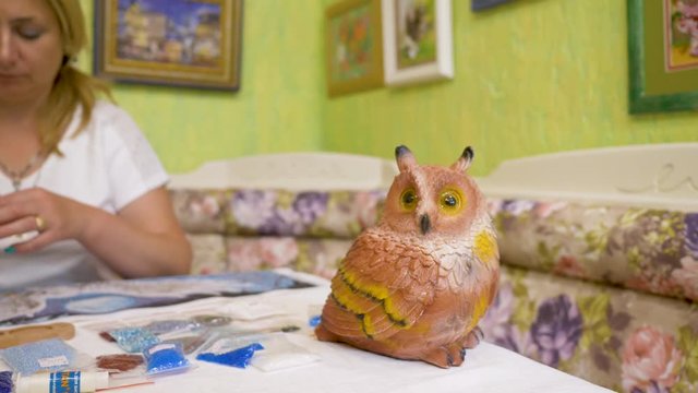Bead Woman embroidering a picture with an owl. Bead embroidery. clay owl statue