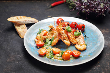 Shrimps in butter sauce with cherry tomatoes. A tasty crustacean dish. A plate with an appetizing dish. Application suggestion. Culinary photography, food stylization.