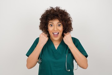 Caucasian young doctor woman rejoicing her success and victory clenching her fists with joy. Lucky woman being happy to achieve her aim and goals.