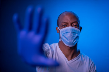 STOP Coronavirus, African American man shows the stop coronavirus sign, wearing protective mask and gloves on blue background in studio. Focus on face. COVID-19 concept.